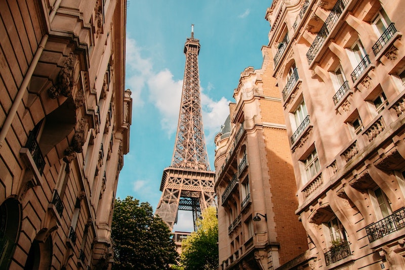 The Eiffel Tower showing between two buildings with a blue sky behind it